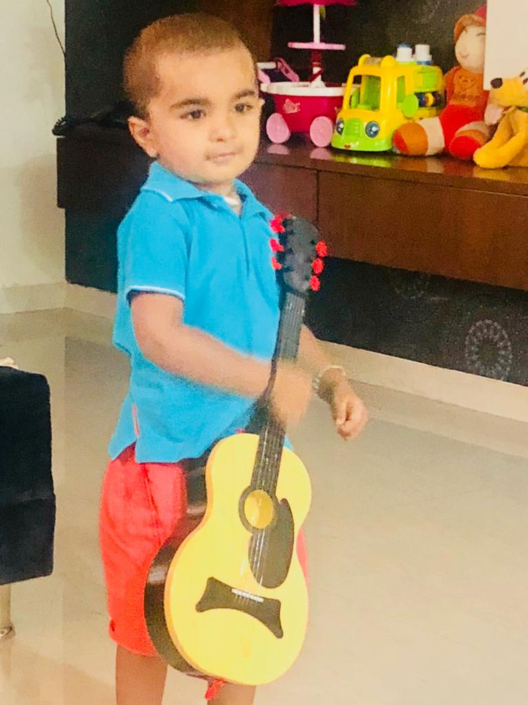 Young Hridan in a blue shirt holding a small yellow guitar
