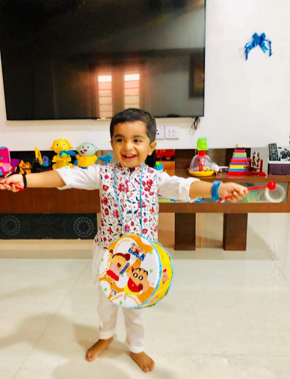Young Hridan smiling with a colourful toy drum and holding two drumsticks